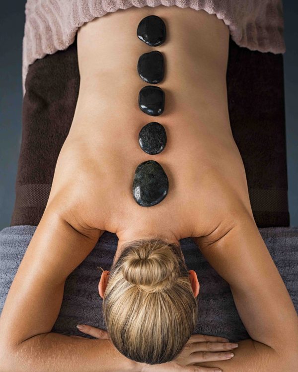 Top view of mature woman relaxing during hot stone massage. High angle view of senior woman back in a wellness spa receiving lastone therapy. Senior woman enjoying a hot stone treatment.